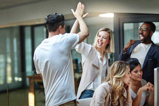 We've done it again! Shot of a group of colleagues giving each other a high five while using a computer together at work happiness stock pictures, royalty-free photos & images