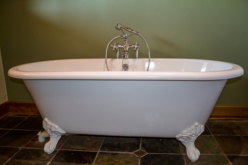 Vintage type footed white bath tub in olive green bathroom with slate tile floor
