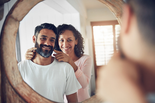 Shot of a mature man looking at his reflection in the mirror with his wife encouraging him to smile