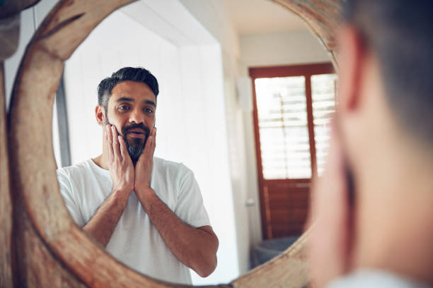 Who is this man I've become? Shot of a mature man looking at his reflection the bathroom mirror low self esteem stock pictures, royalty-free photos & images
