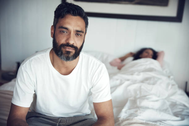 I miss her when she sleeps in Portrait of a mature man looking upset while his wife sleeps in the background ignoring photos stock pictures, royalty-free photos & images