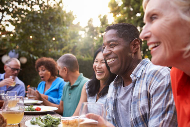 gruppo di amici maturi che si godono il pasto all'aperto nel cortile di casa - festa in giardino foto e immagini stock