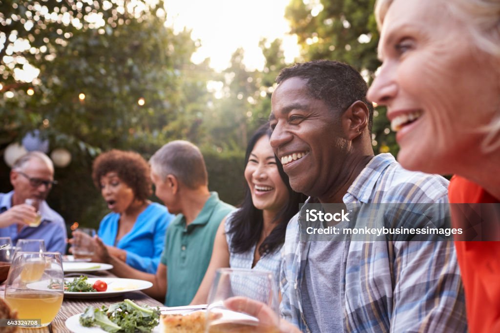 Group Of Mature Friends Enjoying Outdoor Meal In Backyard Eating Stock Photo