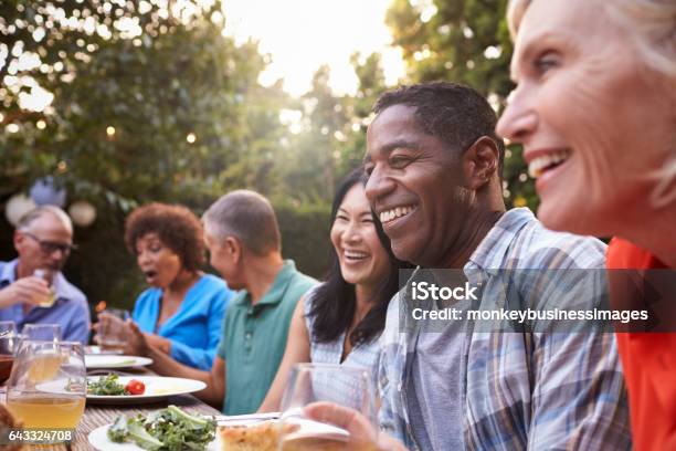 Group Of Mature Friends Enjoying Outdoor Meal In Backyard Stock Photo - Download Image Now