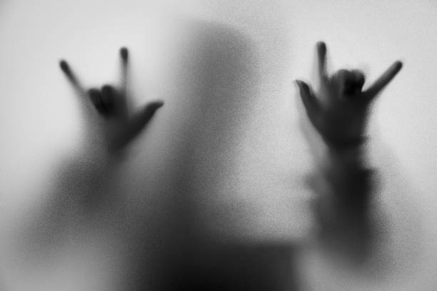 Shadow blur of horror man in jacket with hood.Hands do as a symbol love on the glass.Dangerous man behind the frosted glass.Mystery man.Halloween background.Black and white picture.Blur picture desenfoque de sombra del hombre de horror en la chaqueta con capucha. manos como un símbolo de amor en el vidrio. hombre peligroso tras el cristal helado. misterio del hombre. fondo de halloween. foto blanco y negro. desenfoque de imagen