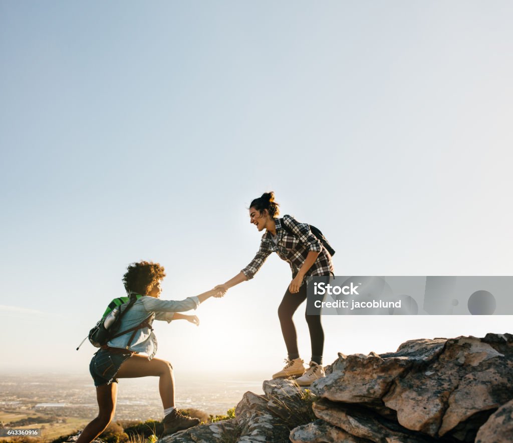 Female friends hiking help each other in mountains Female friends hiking help each other in mountains. Young female hiker helping friend while trekking in mountain. Women Stock Photo