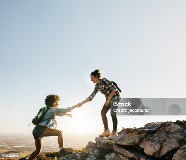 Female Friends Hiking Help Each Other In Mountains Stock Photo - Download Image Now - Women, Hiking, Only Women