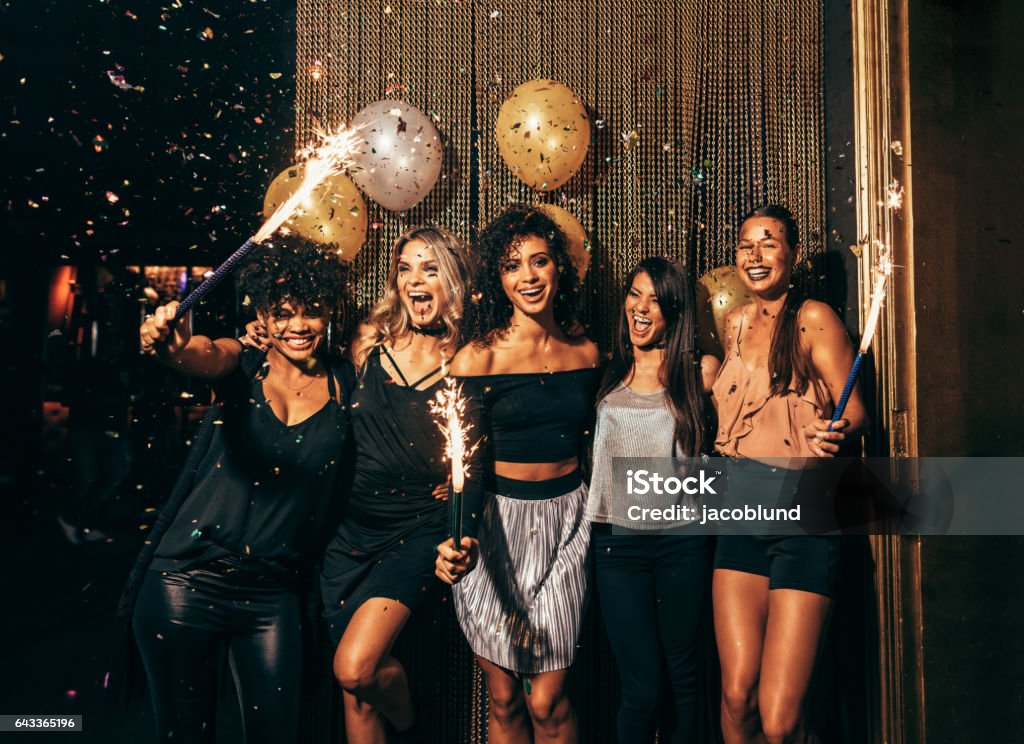 Group of friends partying in nightclub Shot of group of young women celebrating new years eve at the pub. Group of female friends with sparklers partying in nightclub. Party - Social Event Stock Photo