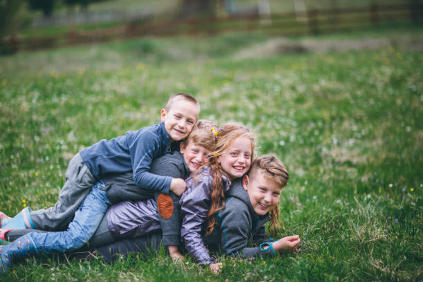 A small group of young children are seen running down a grassy hill with their arms out like airplanes as they enjoy the fresh air.  They are each dressed casually and are laughing and smiling.