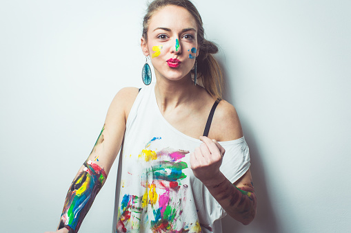 Woman having fun while painting her hands shirt and face with watercolors