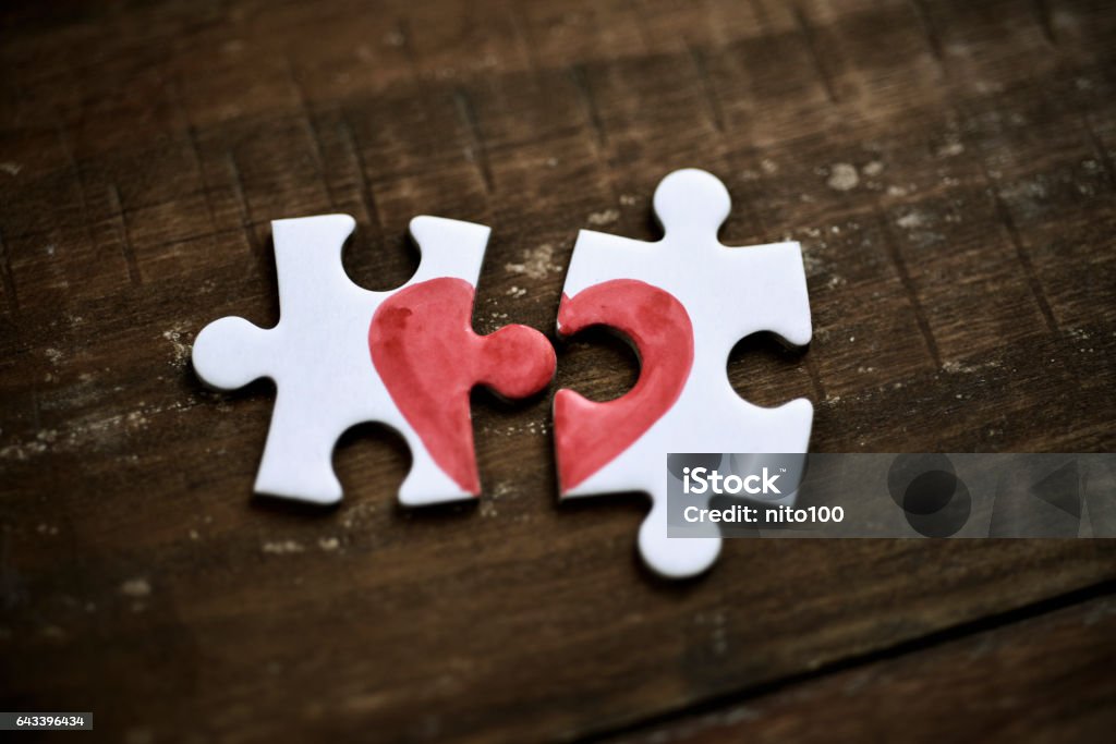 puzzle pieces which form a heart closeup of two separated pieces of a puzzle which together form a heart on a rustic wooden surface, depicting the idea of rupture or cooperation Broken Heart Stock Photo