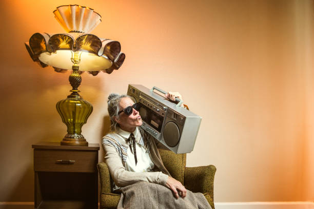 Grandma Using Multiple Modern Electronics A senior elderly woman sits in her vintage, old fashioned styled living room looking at a laptop, a digital touch screen tablet, and a smart phone all at the same time. She smiles as she views a social networking site or email on the internet. rocking chair stock pictures, royalty-free photos & images
