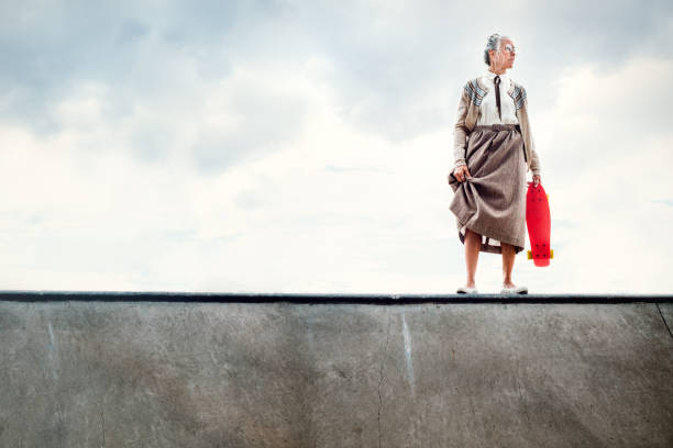 Courageous Grandma Skateboarding A senior woman attempting to skateboard at a skatepark stands at the edge of a halfpipe debating whether to drop in.   A humorous depiction of being young at heart, exercising with extreme sports even in your 80's. conceptual realism photos stock pictures, royalty-free photos & images