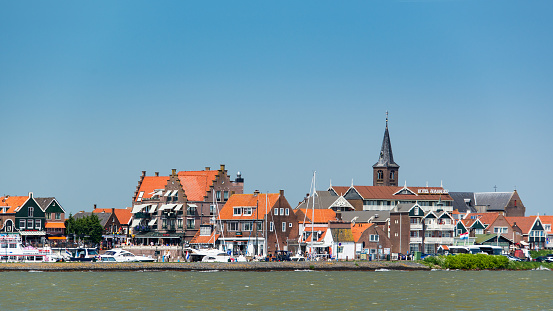 View over water of the Dyke. The famous tourist street in Volendam with souvenir shops, cafes and fish restaurants. Volendam is a historic fishing village on the Ijselmeer in North Holland.