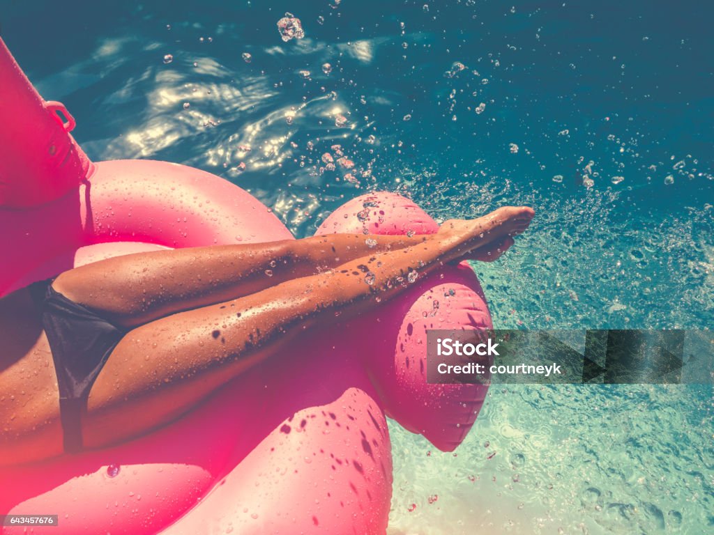 Woman floating on a pink inflatable in swimming pool. Woman floating on a pink inflatable in swimming pool. Tight crop showing only her legs and feet. She is tanned in turquoise water with water splashing onto her. Beach Stock Photo