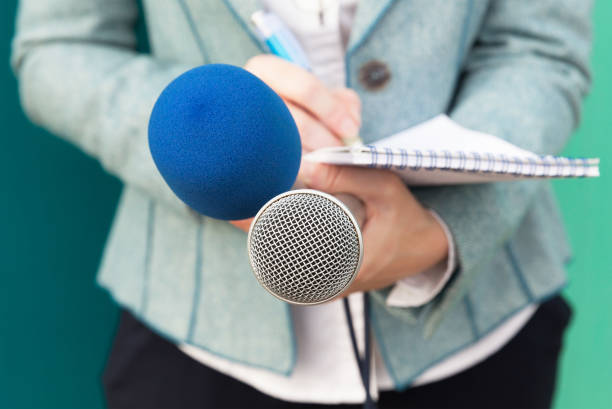 istock Female journalist at news conference, writing notes, holding microphone 643460058
