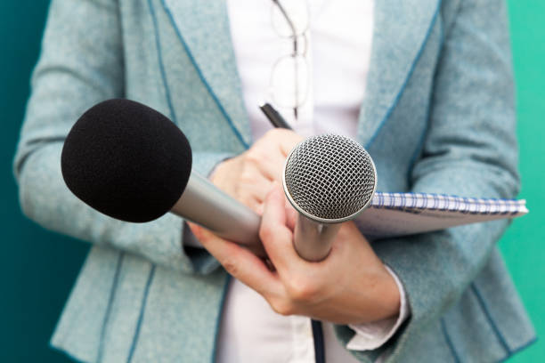 istock Female reporter at press conference, writing notes, holding microphones 643460274