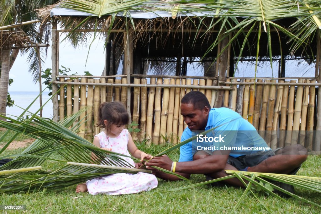 Indigenous Fijian man teaches girl how to create basket Indigenous Fijian man teach young tourist girl how to create a basket from weaving a Coconut Palm leaves.Travel Fiji concept, Real people copy space Fiji Stock Photo