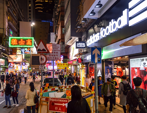 This is a busy street in Hong Kong with colorful signs, many pedestrians, and continuous vehicular activity.