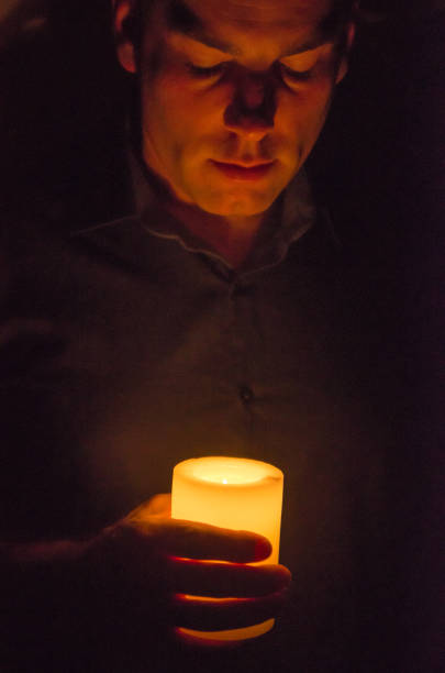 Hand holding a lit candle in darkness\n