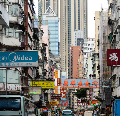 This is a busy street in Hong Kong with colorful signs, many pedestrians, and continuous vehicular activity.