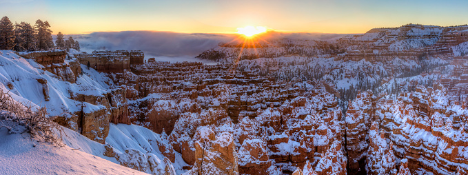 The sun rises out of the a fog bank over the Silent City of snow shrouded hoodoos and Sunset Point in Bryce Canyon National Park, Utah