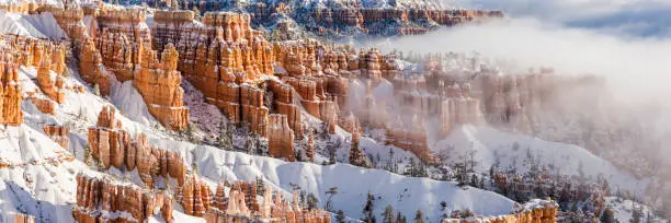 Panoramic image of fog and low hanging clouds partially cover snow-capped hoodoos Bryce Canyon National Park, Utah (Panorama)