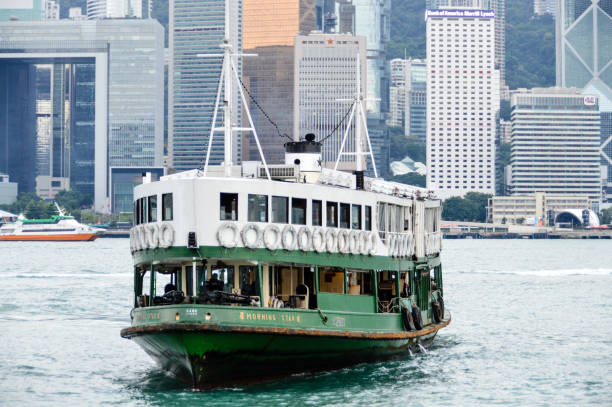 The iconic green and white Star Ferry chugging across the blue waters of Hong Kong Harbour overlooked by the crowded downtown cityscape of Hong Kong Island.