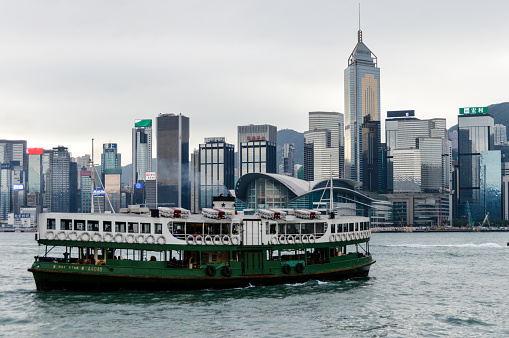 The iconic green and white Star Ferry chugging across the blue waters of Hong Kong Harbour overlooked by the crowded downtown cityscape of Hong Kong Island.
