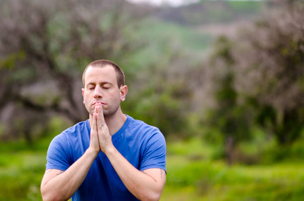 Man wearing a blue shirt praying alone in nature embracing God`s creation.