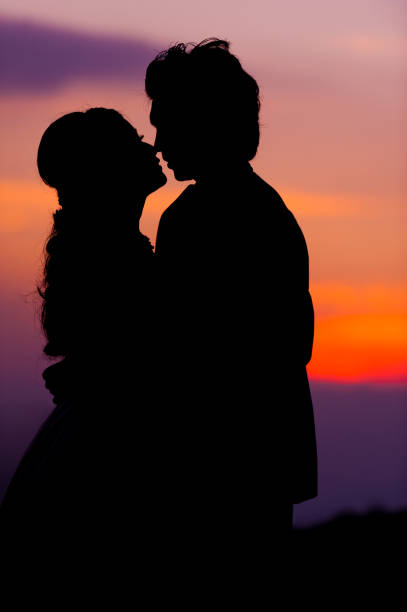 silhouette of embracing asian bride and groom at sunset - silhouette kissing park sunset imagens e fotografias de stock