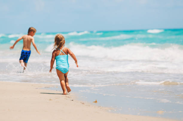 istock little girl and boy run play with waves on beach 643583008