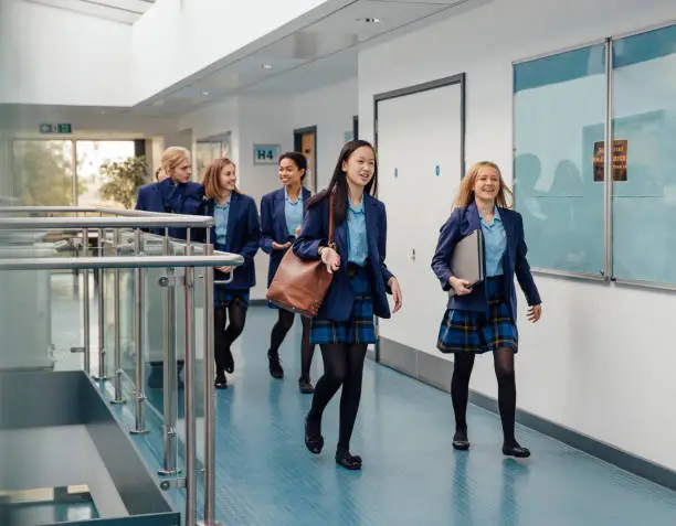 Group of students are walking down the school corridor together wearing uniform.