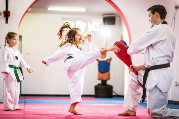 Two cute girls on taekwondo training, kicking and learning self-defence Taekwondo training in sport hall with tatami. Taekwondo is equally popular sport among girls and boys, young men and women. Sport develops physique and strength on lower and upper limbs equally. taekwondo photos stock pictures, royalty-free photos & images