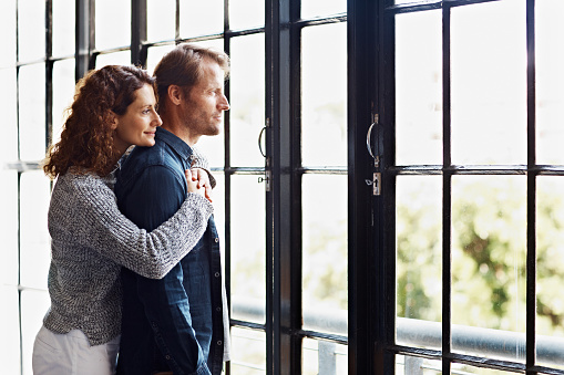 Shot of an affectionate mature couple hugging in front of a window at home