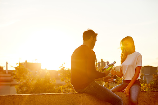 Shot of a smiling couple drinking champagne while sitting on their rooftop at sunset