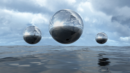3D illustration of transparent liquid balls hoovering above water. A close-up of abstract organic elements. Silver shiny colored textures with a lot of reflection.