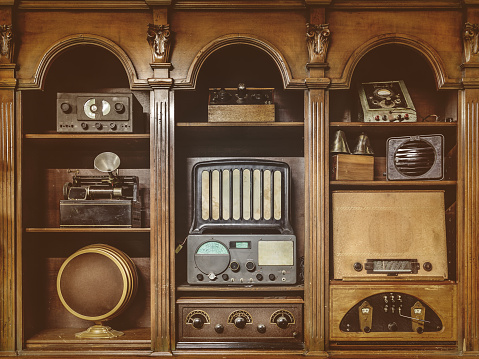 Sepia toned image of old radio's in a wooden cabinet