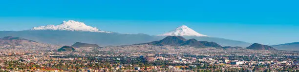 Panoramic stock photo of the snow covered Iztaccihuatl aka Ixtaccihuatl (left) and Popocatepetl (right) volcanic mountains with Mexico City at their feet as seen from Mexico City, Mexico.