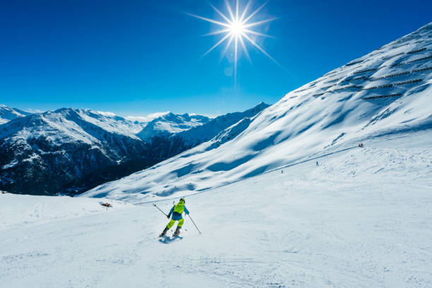Young skier skiing down the slope of ski resort on sunny winter day.
