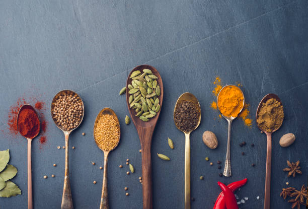 Variety of herbs and spices on slate background. Many are held on metal and wooden spoons. There is also a chilli pepper.