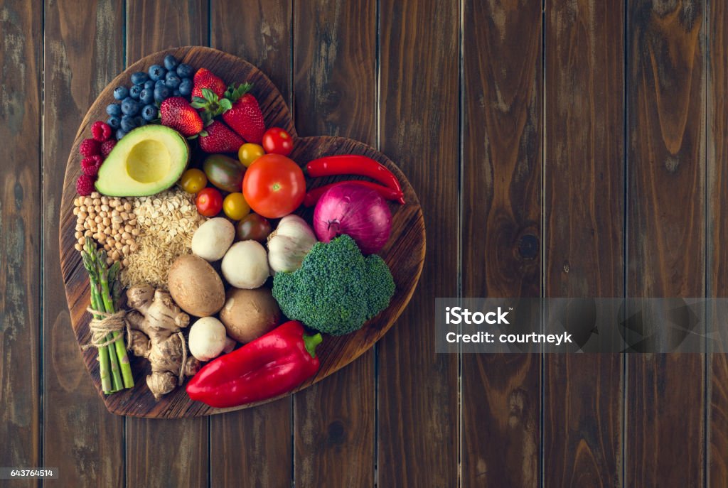 Healthy food on a heart shape cutting board Healthy food on a heart shape cutting board. Love of food concept with fruit, vegetables, grains and high fibre foods. Rustic wood textures Heart Shape Stock Photo
