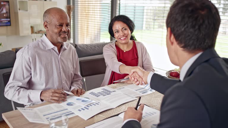 Senior couple shaking hands with a personal banker advising them in their home