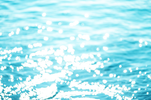 Summer Background with sparkling natural bokeh over blue water / Soft focus bokeh light effects