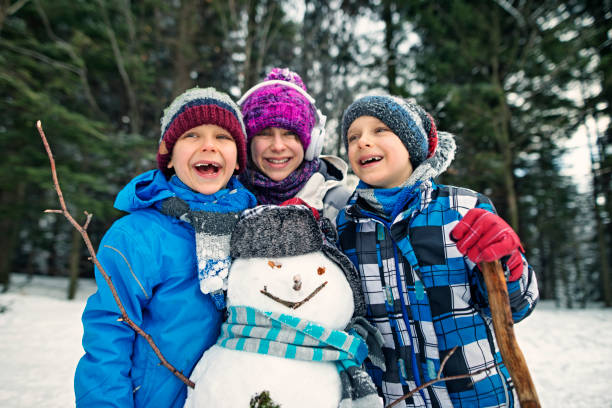 Portrait of little girl and little boys posing with a snowman. Kids are laughing and embracing and having a lot of fun.