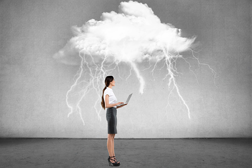 Businesswoman working on laptop in front of wall with thundercloud