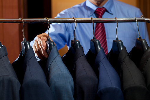 many suits hanging on rack with a man hand