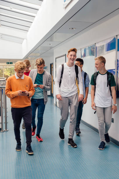 Friends Going To Lessons Group of teenage boys are walking to their next school lesson together. They are talking and laughing as they walk and some of the students are using smart phones. teenagers only teenager multi ethnic group student stock pictures, royalty-free photos & images
