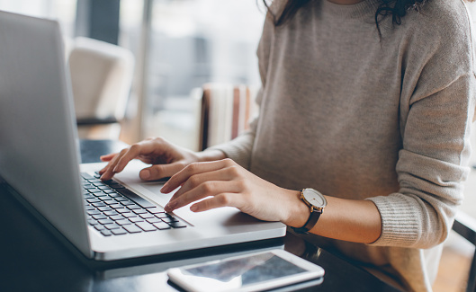 Cropped image of a man, freelancer, businessman, or call center worker working while sitting at a laptop at a desk in an office or coworking space. Remote work from home.