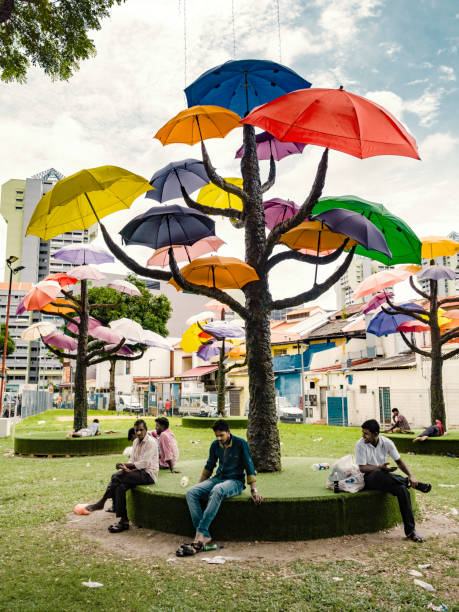 Group of men resting in a park with trees with umbrellas that provide shadow under the tropical heat of Singapore.. The art installation designed by Ms Marthalia Budiman is part of a new initiative in the city to bring artistic projects and performances to little India
